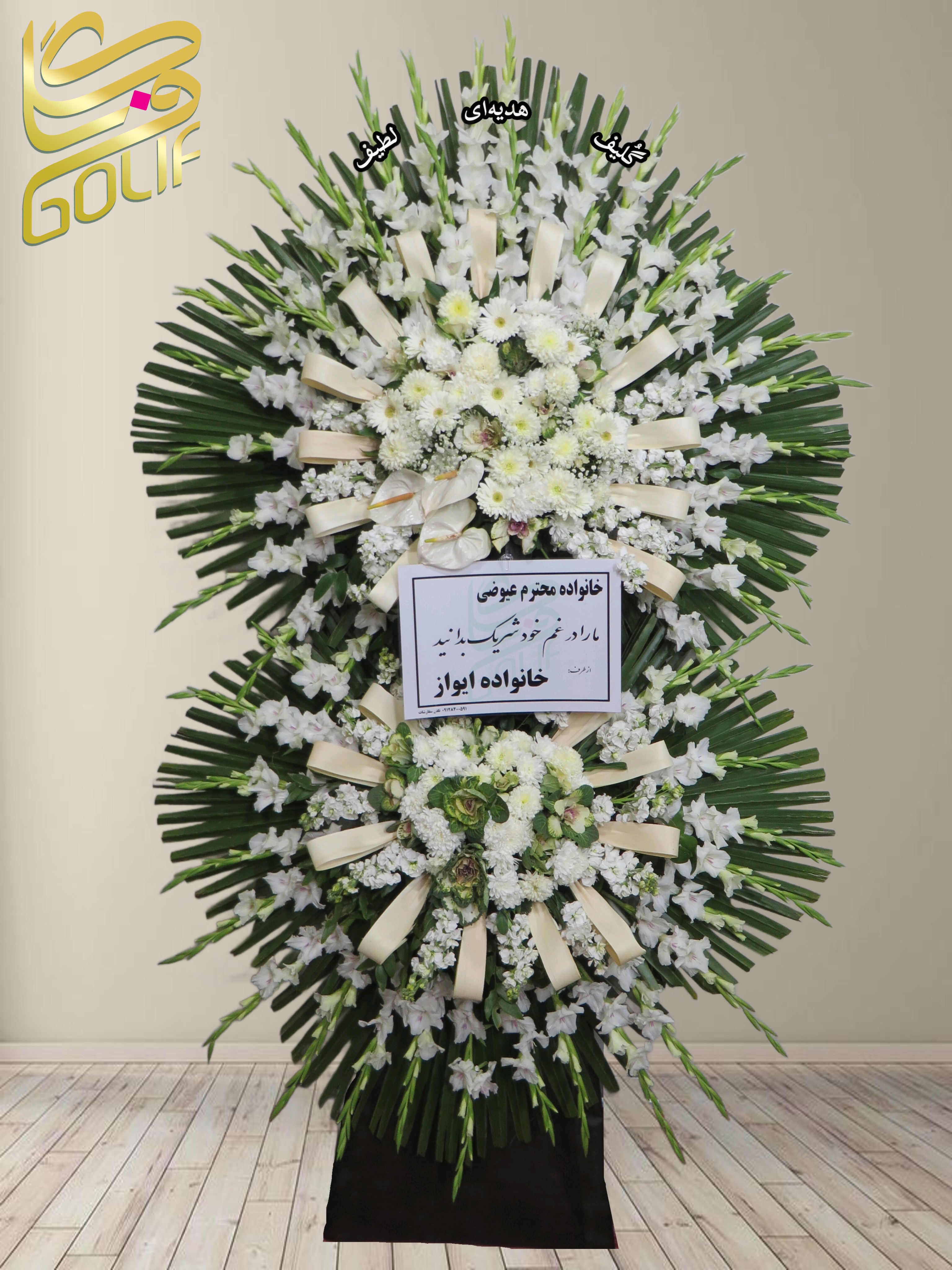 تاج گل تسلیت دو طبقه (گلایل، داوودی) تاج گل ختم، تاج گل ترحیم، تاج گل مراسم ترحیم در این تاج گل، از ترکیبی از گل‌های سفید و سبز با طراحی رسمی و باشکوه استفاده شده است. گل‌های به‌کاررفته شامل موارد زیر هستند: ✅ گل گلایل سفید: یکی از پرکاربردترین گل‌ها در تاج گل ترحیم، که نماد پاکی، یادبود و همدردی است. ✅ گل داوودی سفید: سمبل صداقت، احترام و آرامش، که حضور آن در مراسم ترحیم بسیار رایج است. ✅ گل لیسیانتوس سفید: این گل به لطافت و ظرافت شهرت دارد و نماد همدلی و عشق پاک است. ✅ آنتوریوم سبز: این گل جلوه‌ای خاص به تاج گل می‌بخشد و سمبل احترام و قدرت است. ✅ برگ‌های تزئینی (نخل و سایر برگ‌های سبز): برای حجم‌دهی و افزایش شکوه تاج گل استفاده شده است. ✅ روبان‌های کرم یا سفید: برای تزئین و جلوه‌ی بیشتر در طراحی این تاج گل به کار رفته‌اند. این ترکیب باعث شده که تاج گل جلوه‌ای بسیار شیک، رسمی و مناسب برای مراسم ترحیم داشته باشد. اگر توضیحات بیشتری مدنظر دارید، بفرمایید! سفارش آنلاین تاج گل سفارش آنلاین گل عکاسی شده توسط گل‌فروشی آنلاین گلیف