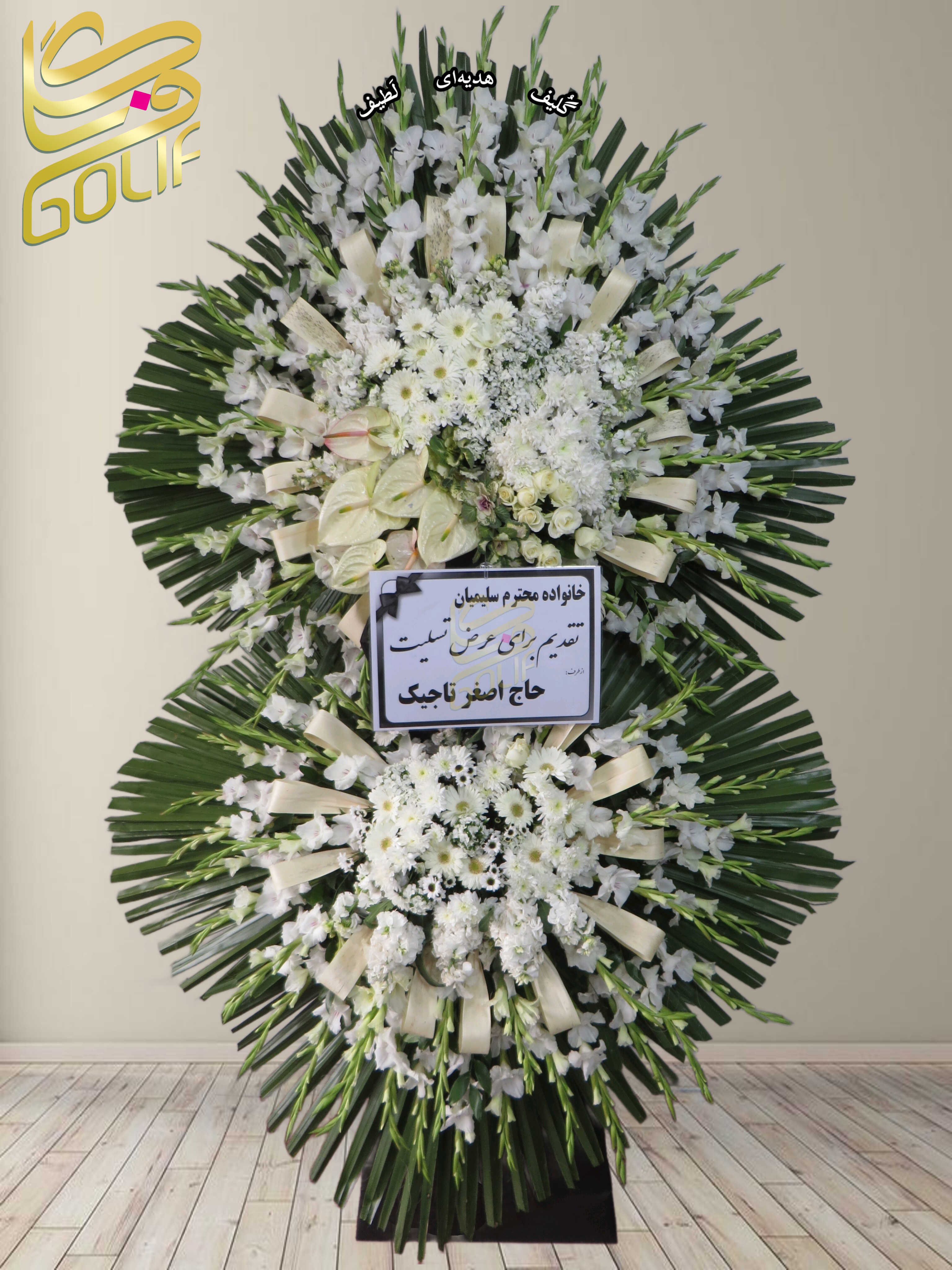 تاج گل تسلیت دو طبقه (گلایول، داوودی، میخک) تاج گل ختم، تاج گل ترحیم، تاج گل مراسم ترحیم گل‌هایی که در این تاج گل دیده می‌شوند شامل موارد زیر هستند: گلایول: گل‌های سفید بلند و جذاب که معمولاً برای مراسم تسلیت مناسب هستند. داوودی: گل‌هایی سفید که به طور گسترده‌ای در تاج گل‌های رسمی به کار می‌روند. میخک سفید: گل‌های ساده و زیبا که جلوه خاصی به طراحی تاج گل می‌دهند. این گل‌ها در کنار برگ‌های سبز به صورت دایره‌ای طراحی شده‌اند. سفارش آنلاین تاج گل سفارش آنلاین گل عکاسی شده توسط گل‌فروشی آنلاین گلیف