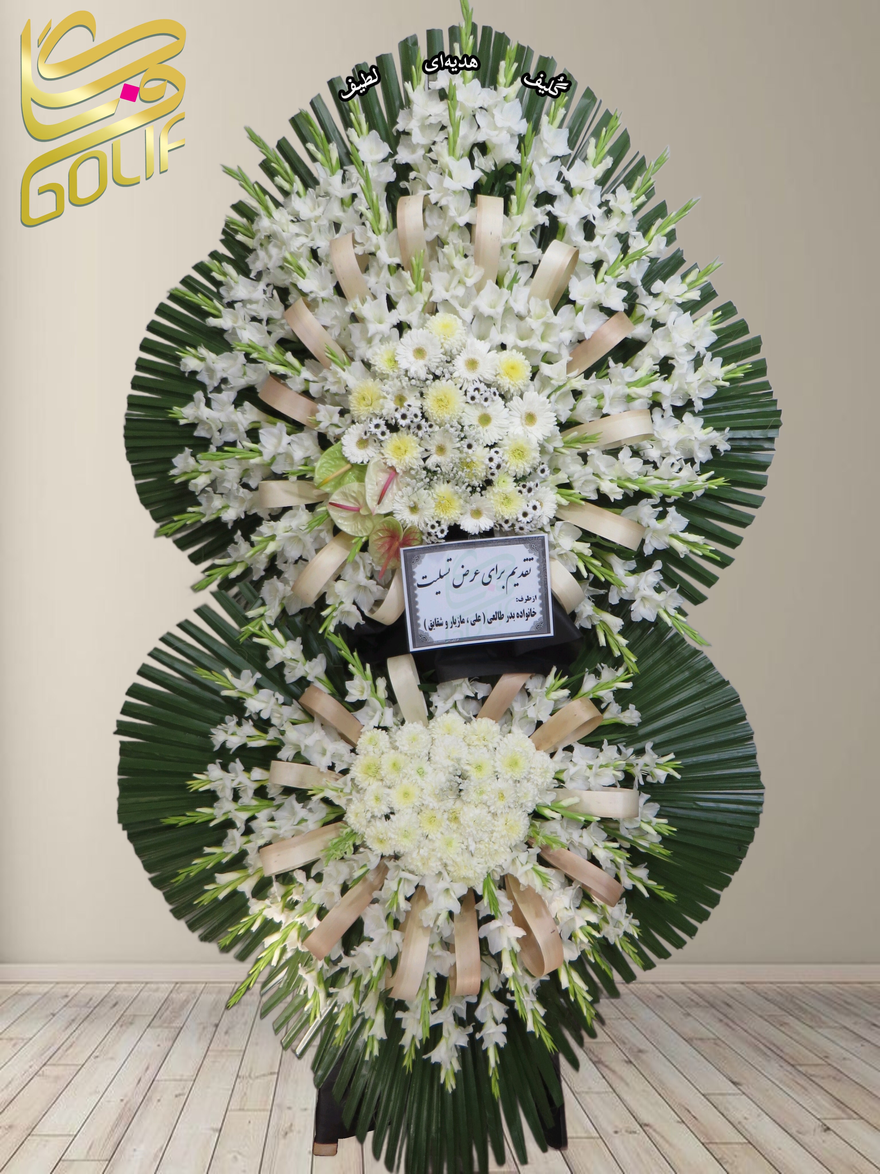 تاج گل تسلیت دو طبقه (گلایول, ژربرا) تاج گل ختم، تاج گل ترحیم، تاج گل مراسم ترحیم گل‌هایی که در این تاج گل دیده می‌شوند شامل موارد زیر هستند: گلایول: گل‌های سفید بلند و جذاب که معمولاً برای مراسم تسلیت مناسب هستند. ژربرا این گل‌ها در کنار برگ‌های سبز به صورت دایره‌ای طراحی شده‌اند.. سفارش آنلاین تاج گل سفارش آنلاین گل عکاسی شده توسط گل‌فروشی آنلاین گلیف