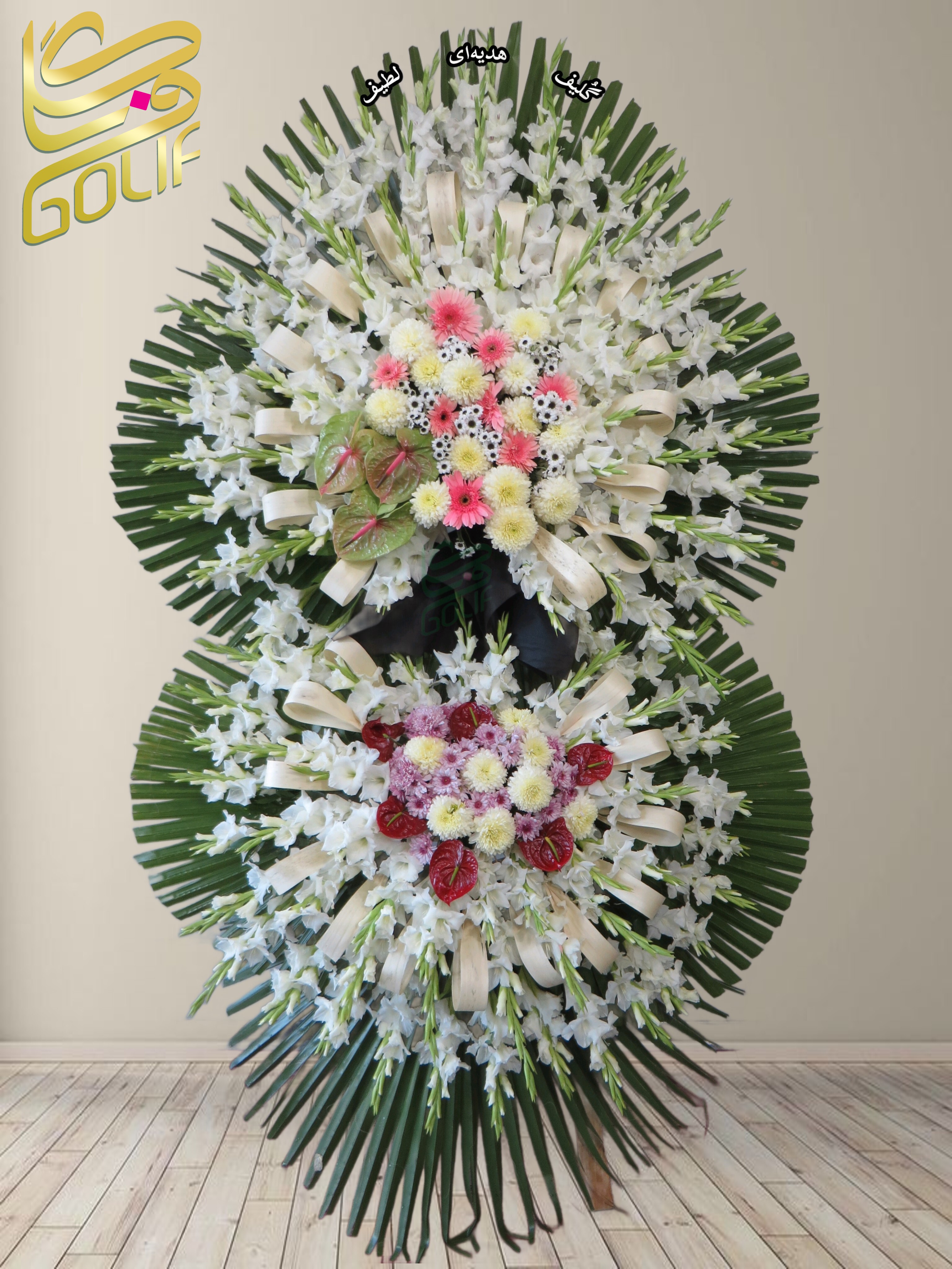 تاج گل تسلیت دو طبقه (گلایول, داوودی, ژربرا, آنتوریوم) تاج گل ختم، تاج گل ترحیم، تاج گل مراسم ترحیم گل‌هایی که در این تاج گل دیده می‌شوند شامل موارد زیر هستند: گلایول: گل‌های سفید بلند و جذاب که معمولاً برای مراسم تسلیت مناسب هستند. ژربرا این گل‌ها در کنار برگ‌های سبز به صورت دایره‌ای طراحی شده‌اند.. سفارش آنلاین تاج گل سفارش آنلاین گل عکاسی شده توسط گل‌فروشی آنلاین گلیف