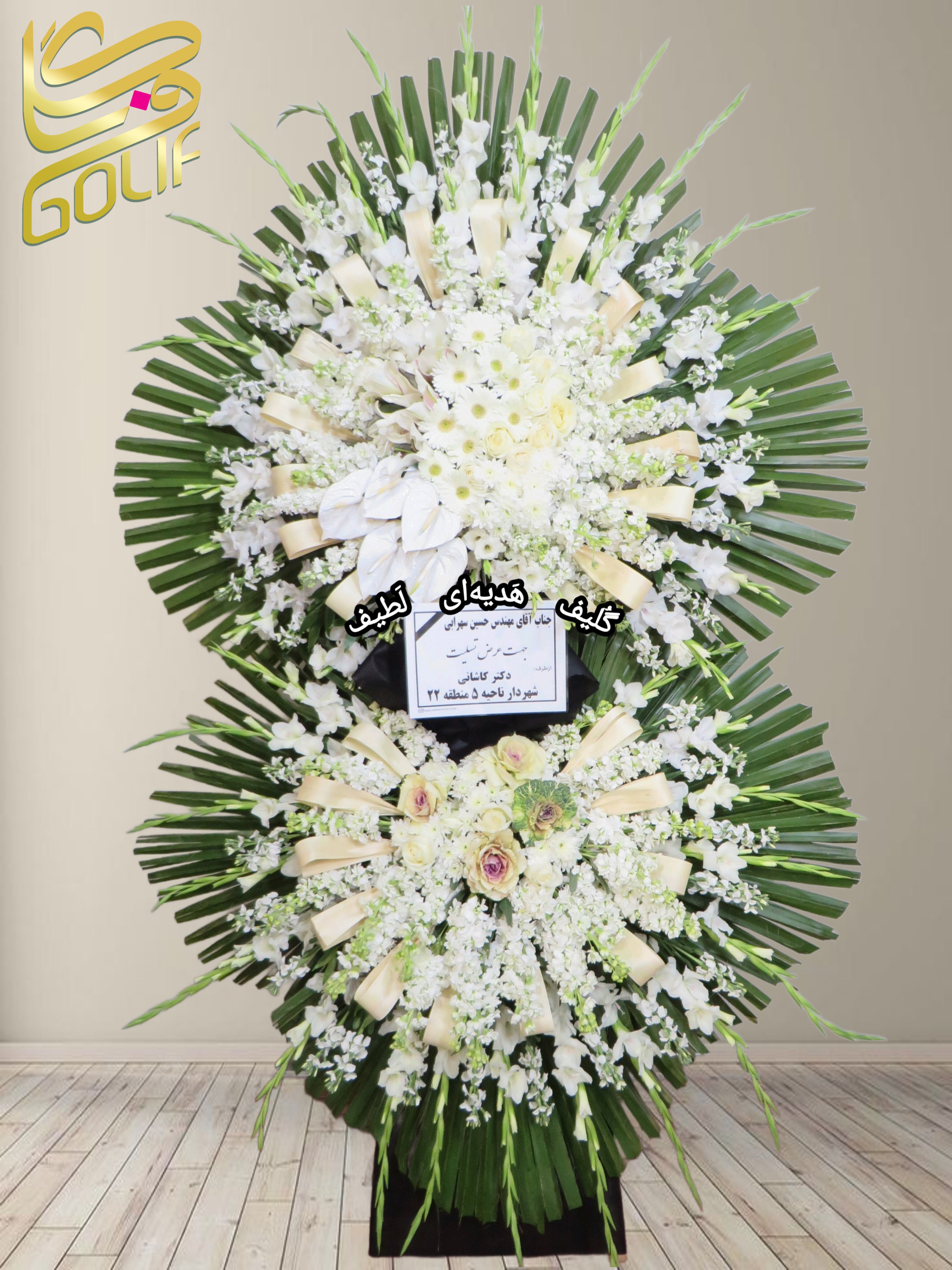 تاج گل تسلیت دو طبقه (گلایول، داوودی، میخک) تاج گل ختم، تاج گل ترحیم، تاج گل مراسم ترحیم گل‌هایی که در این تاج گل دیده می‌شوند شامل موارد زیر هستند: گلایول: گل‌های سفید بلند و جذاب که معمولاً برای مراسم تسلیت مناسب هستند. داوودی: گل‌هایی سفید که به طور گسترده‌ای در تاج گل‌های رسمی به کار می‌روند. میخک سفید: گل‌های ساده و زیبا که جلوه خاصی به طراحی تاج گل می‌دهند. این گل‌ها در کنار برگ‌های سبز به صورت دایره‌ای طراحی شده‌اند. سفارش آنلاین تاج گل سفارش آنلاین گل عکاسی شده توسط گل‌فروشی آنلاین گلیف