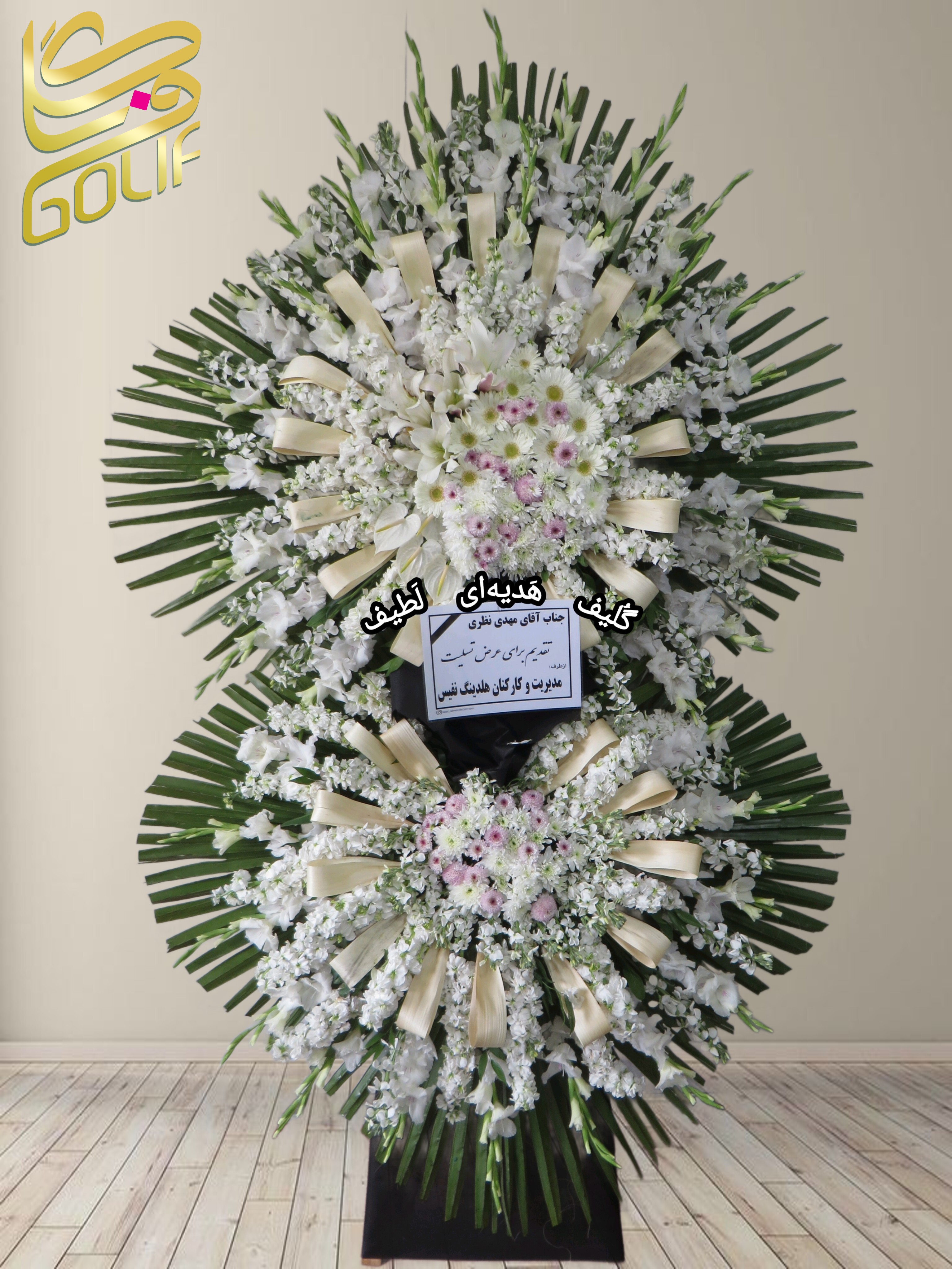 تاج گل تسلیت دو طبقه (گلایول, داوودی, ژربرا, آنتوریوم) تاج گل ختم، تاج گل ترحیم، تاج گل مراسم ترحیم گل‌هایی که در این تاج گل دیده می‌شوند شامل موارد زیر هستند: گلایول: گل‌های سفید بلند و جذاب که معمولاً برای مراسم تسلیت مناسب هستند. ژربرا این گل‌ها در کنار برگ‌های سبز به صورت دایره‌ای طراحی شده‌اند.. سفارش آنلاین تاج گل سفارش آنلاین گل عکاسی شده توسط گل‌فروشی آنلاین گلیف