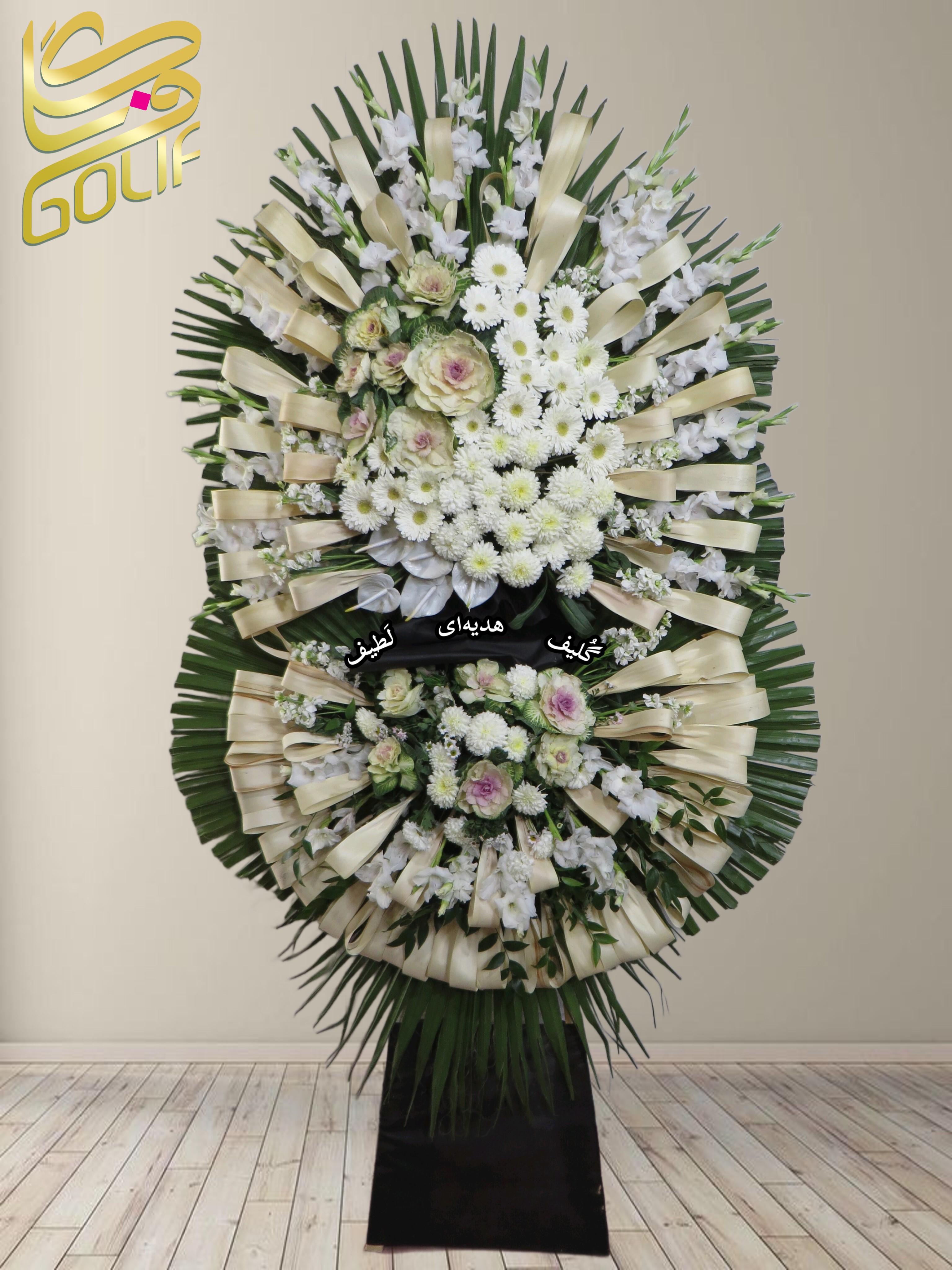 تاج گل تسلیت دو طبقه (گلایل، داوودی) تاج گل ختم، تاج گل ترحیم، تاج گل مراسم ترحیم در این تاج گل ترحیم از ترکیب گل‌های سفید و کرم با طراحی رسمی و شیک استفاده شده است. گل‌های به‌کاررفته شامل موارد زیر هستند: ✅ **گل گلایل سفید:** نماد پاکی، همدردی و احترام، یکی از رایج‌ترین گل‌ها در مراسم ترحیم. ✅ **گل داوودی سفید:** سمبل صداقت، آرامش و یادبود، که در تاج گل‌های ترحیم حضوری پررنگ دارد. ✅ **گل رز هلندی کرم با حاشیه صورتی:** این نوع رز نشان‌دهنده عشق، همدردی و خاطرات ماندگار است. ✅ **گل لیسیانتوس سفید:** با ظاهری لطیف و زیبا که نماد همدلی و همراهی در غم و اندوه است. ✅ **برگ‌های تزئینی (نخل و سایر برگ‌های سبز):** برای افزایش شکوه و چشم‌نوازی تاج گل. ✅ **روبان‌های کرم یا سفید:** جهت تزیین و ایجاد جلوه‌ای رسمی و شیک. این ترکیب باعث شده است که تاج گل زیبایی خاصی داشته باشد و برای مراسم‌های ترحیم و یادبود گزینه‌ای ایده‌آل باشد. سفارش آنلاین تاج گل سفارش آنلاین گل عکاسی شده توسط گل‌فروشی آنلاین گلیف