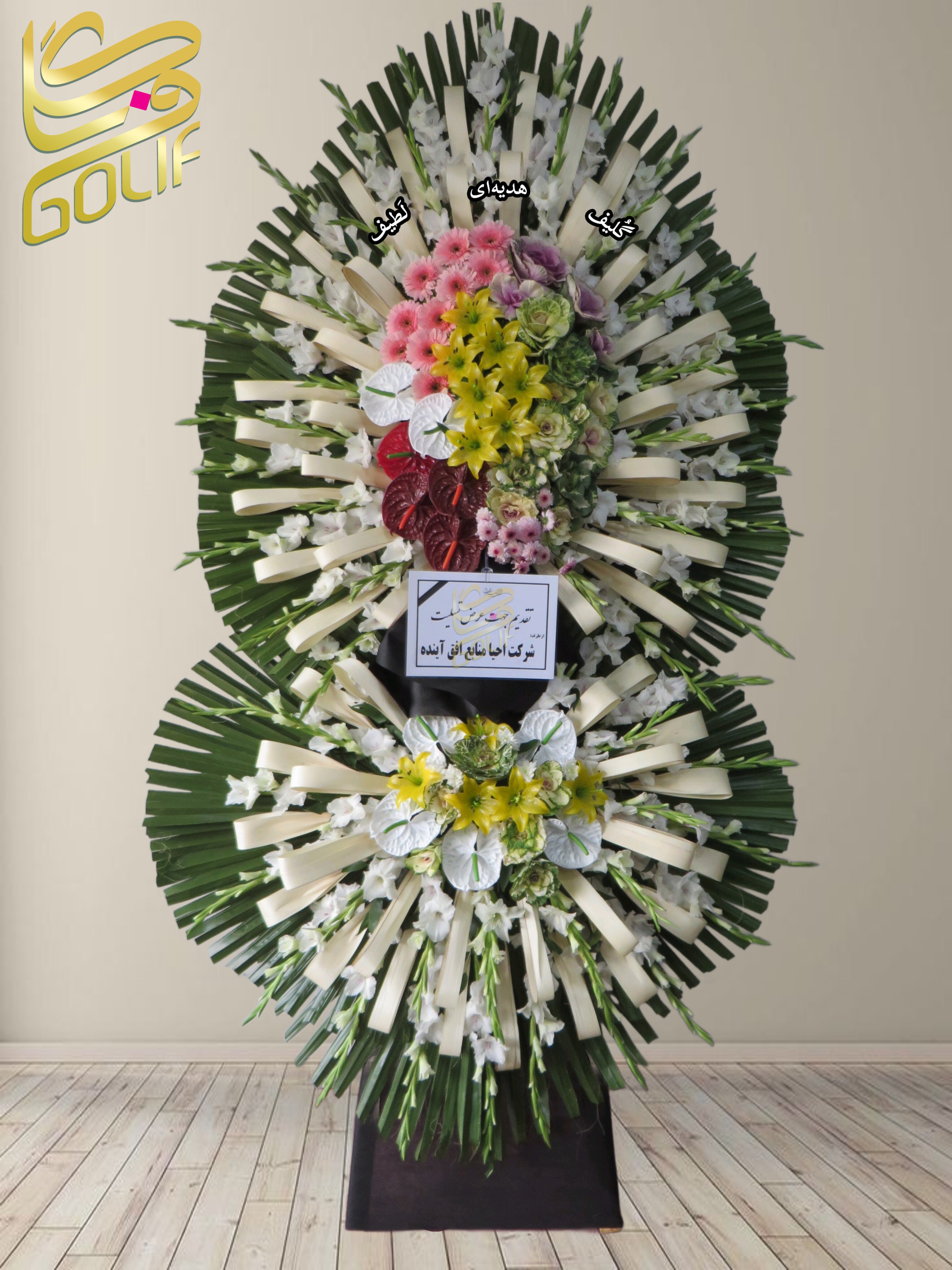 تاج گل تسلیت دو طبقه (لیلیوم، رز، آنتوریوم، گلایل) تاج گل ختم، تاج گل ترحیم، تاج گل مراسم ترحیم گل‌هایی که در این تاج گل دیده می‌شوند شامل موارد زیر هستند: لیلیوم زرد: این گل‌های بزرگ و جذاب در قسمت بالای دسته گل قرار دارند. رزهای صورتی: گل‌های صورتی درخشان که در طراحی دسته گل استفاده شده‌اند. آنتوریوم قرمز: این گل‌های قرمز زیبا در بخش بالایی چیده شده‌اند. گلایل سفید: گل‌های بلند و خوش‌بو در اطراف گل‌ها قرار دارند. آنتوریوم سفید: در بخش پایینی دسته گل استفاده شده‌اند. همچنین برگ‌های سبز و عناصر تزئینی به زیبایی طراحی دسته گل افزوده‌اند.. سفارش آنلاین تاج گل سفارش آنلاین گل عکاسی شده توسط گل‌فروشی آنلاین گلیف